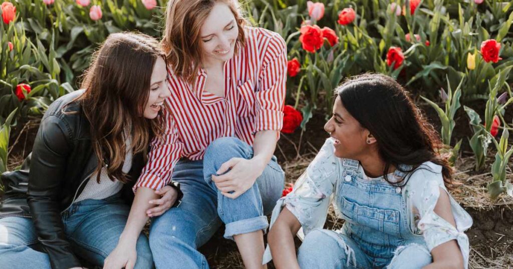 tre amiche ridono sedute in un campo di tulipani